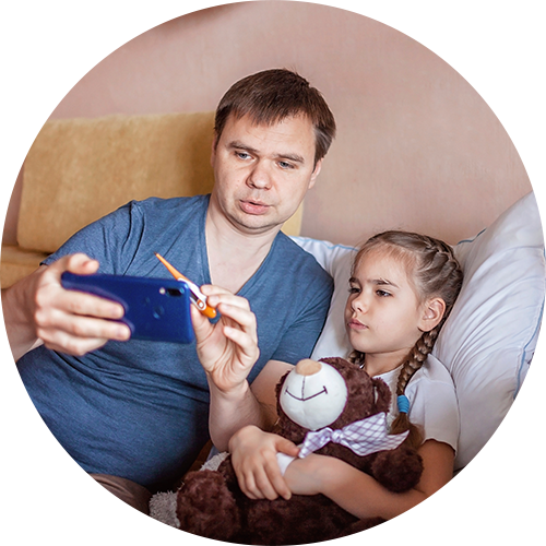 A father with his sick daughter, showing a thermometer to a virtual care call on his cellphone